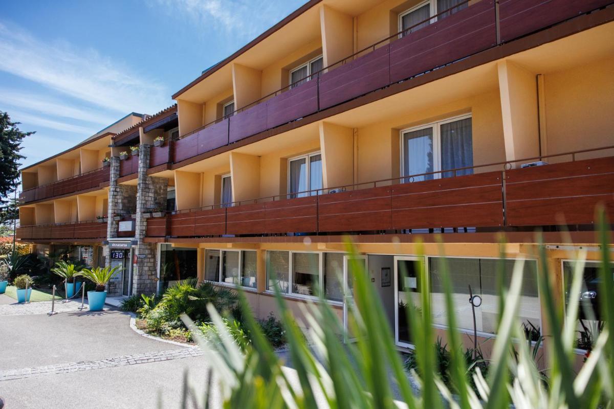 un immeuble d'appartements avec des fenêtres et des plantes au premier plan dans l'établissement Hotel SPA Plage St Jean, à La Ciotat