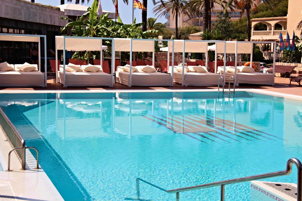 una gran piscina con sillas blancas y un hotel en Hotel Serrano Palace, en Cala Ratjada