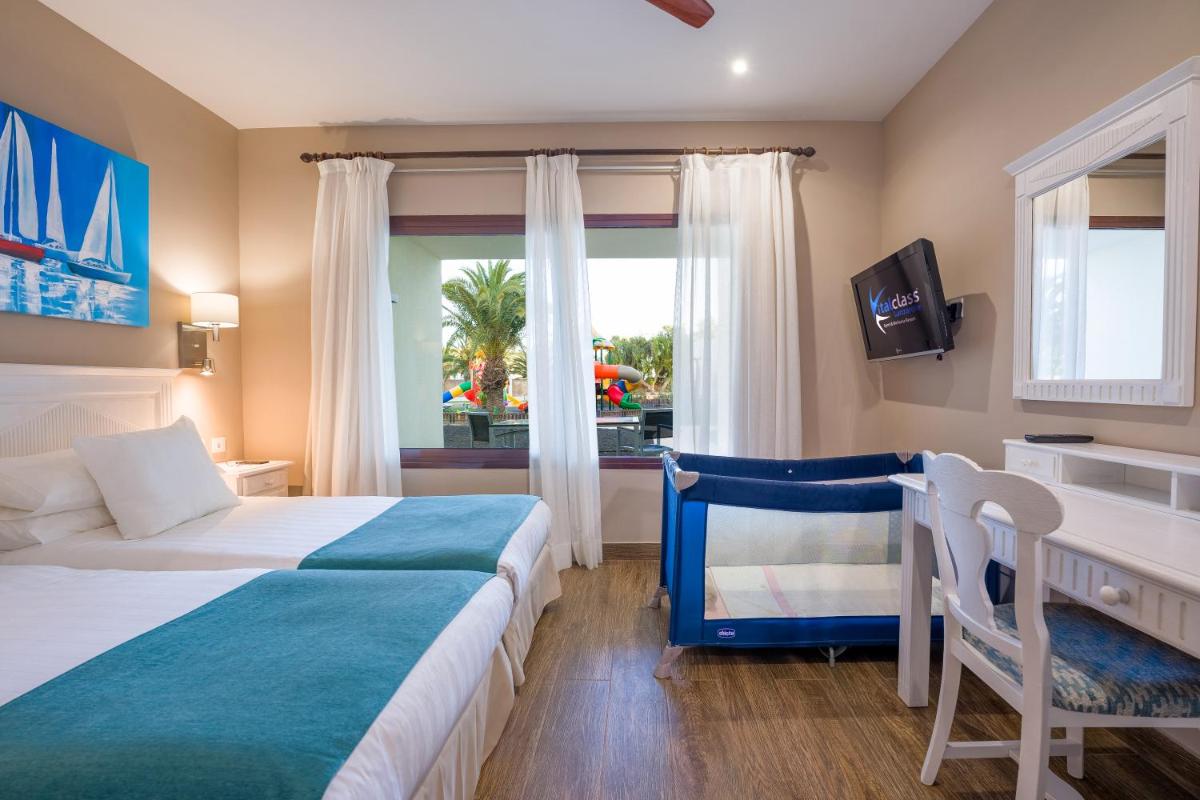 Un dormitorio con dos camas y un escritorio y una ventana. en LANZAROTE PRIME SPORTS by Vitalclass Lanzarote Resort, en Costa Teguise