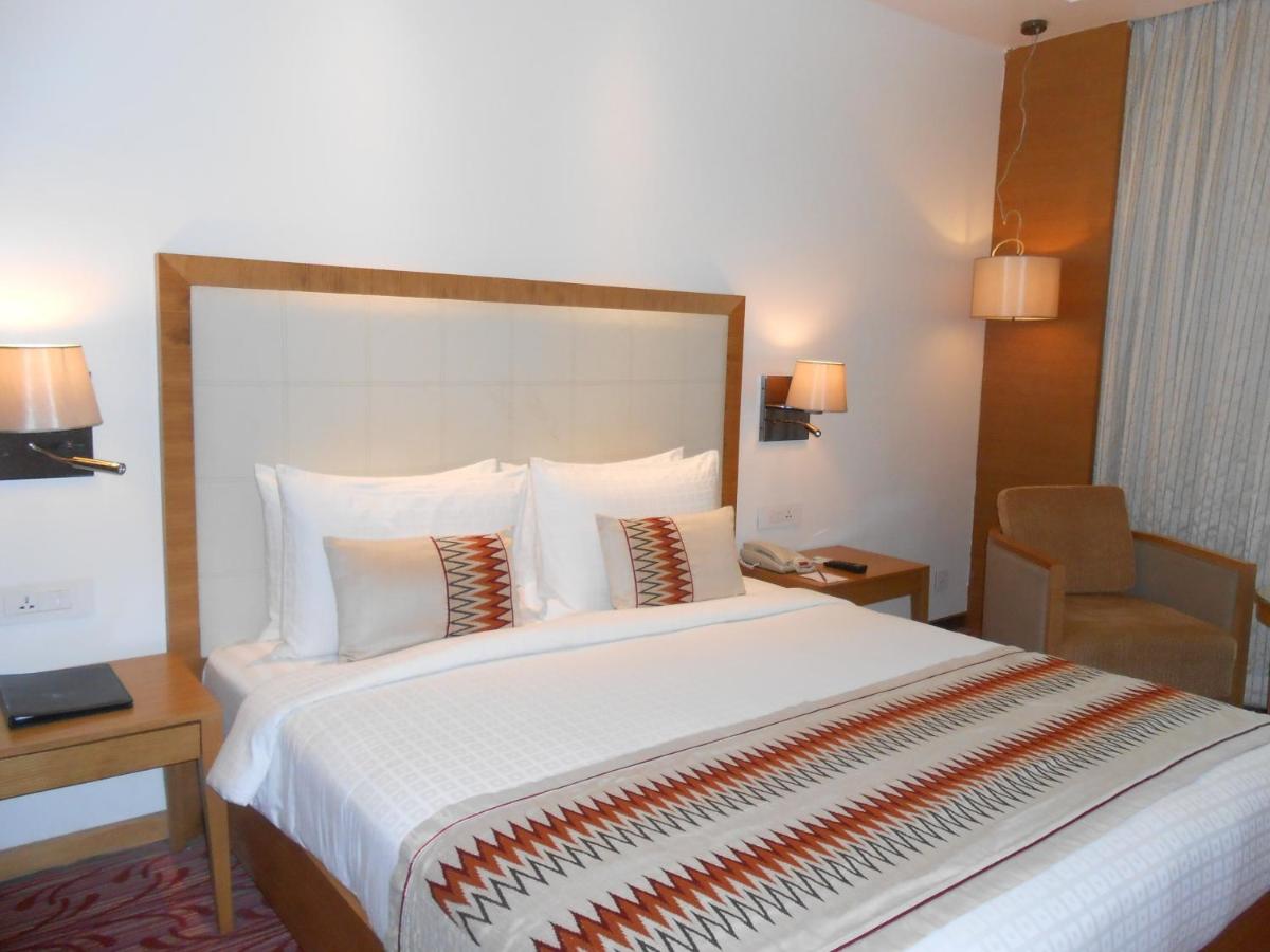 a hotel room with a large bed and a chair at Pride Plaza Hotel, Kolkata in Kolkata