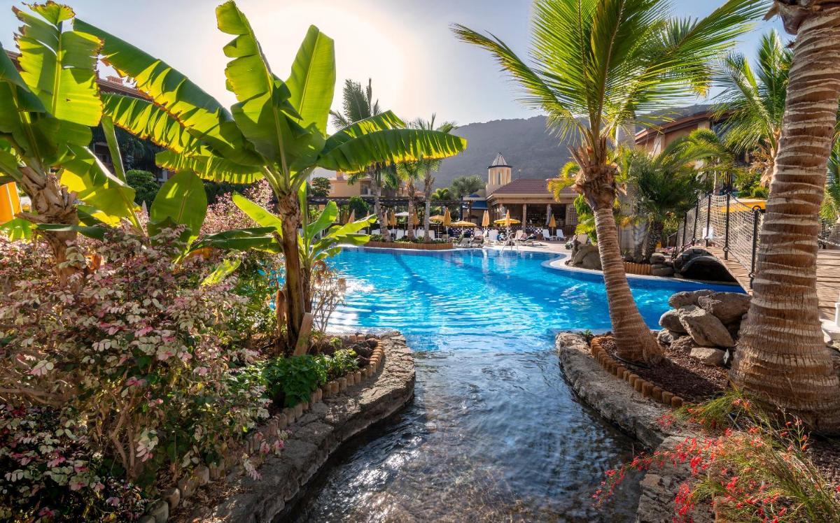 una piscina con palmeras en un resort en Hotel Cordial Mogán Playa, en Puerto de Mogán