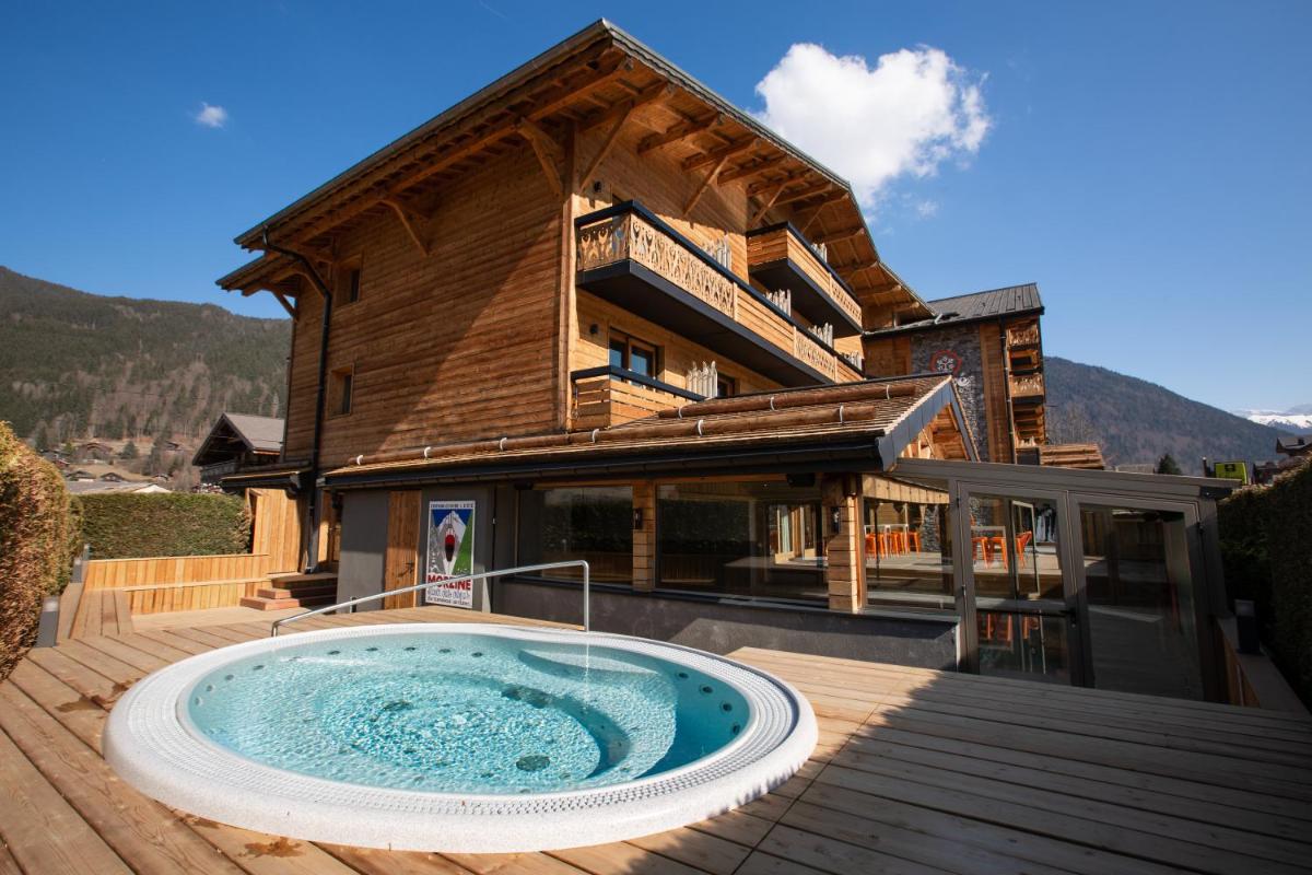 un bain à remous sur une terrasse en face d'une maison dans l'établissement Hôtel Névé, à Morzine