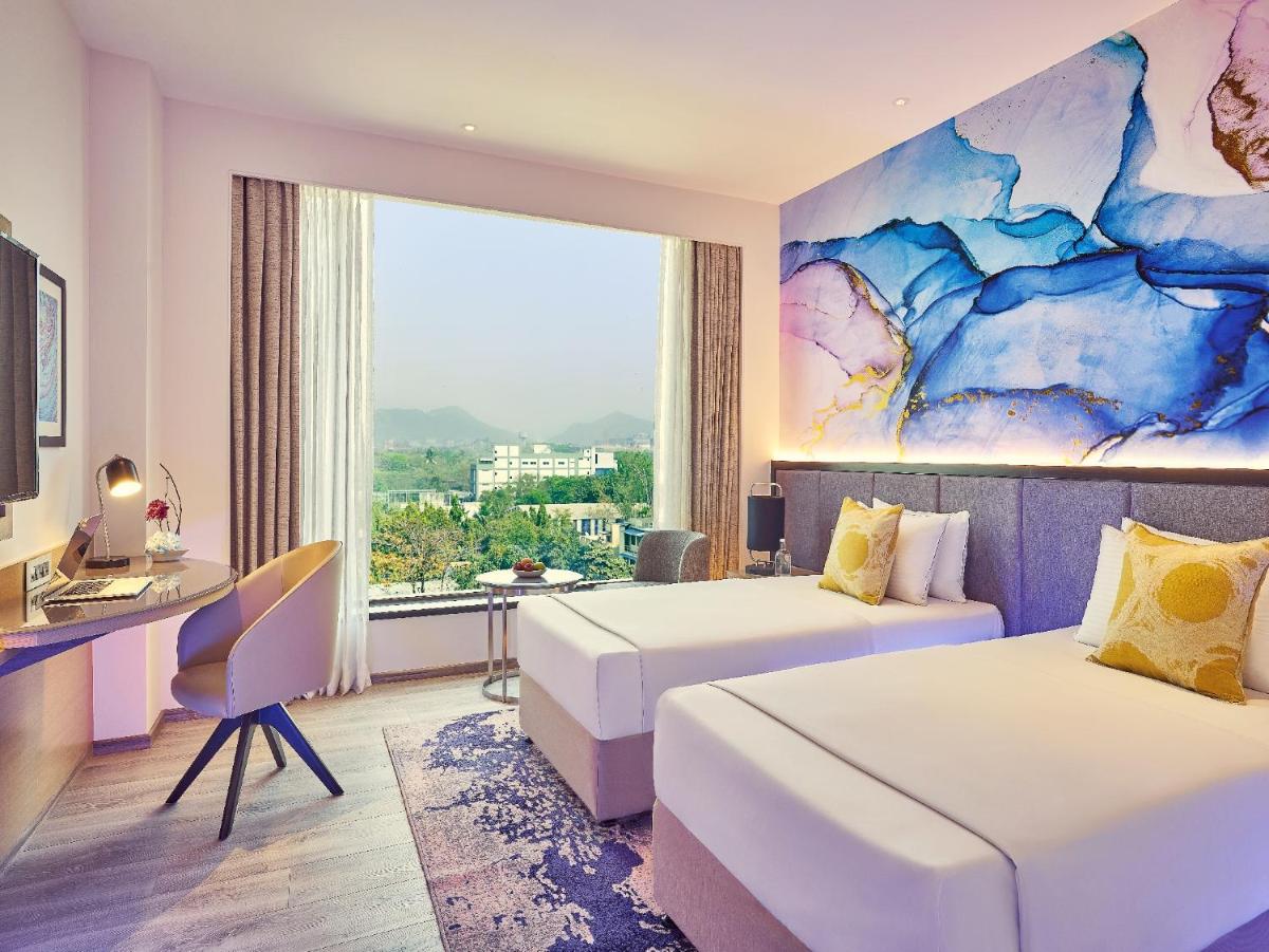 a hotel room with two beds and a desk and a window at Vivanta Navi Mumbai Turbhe in Navi Mumbai