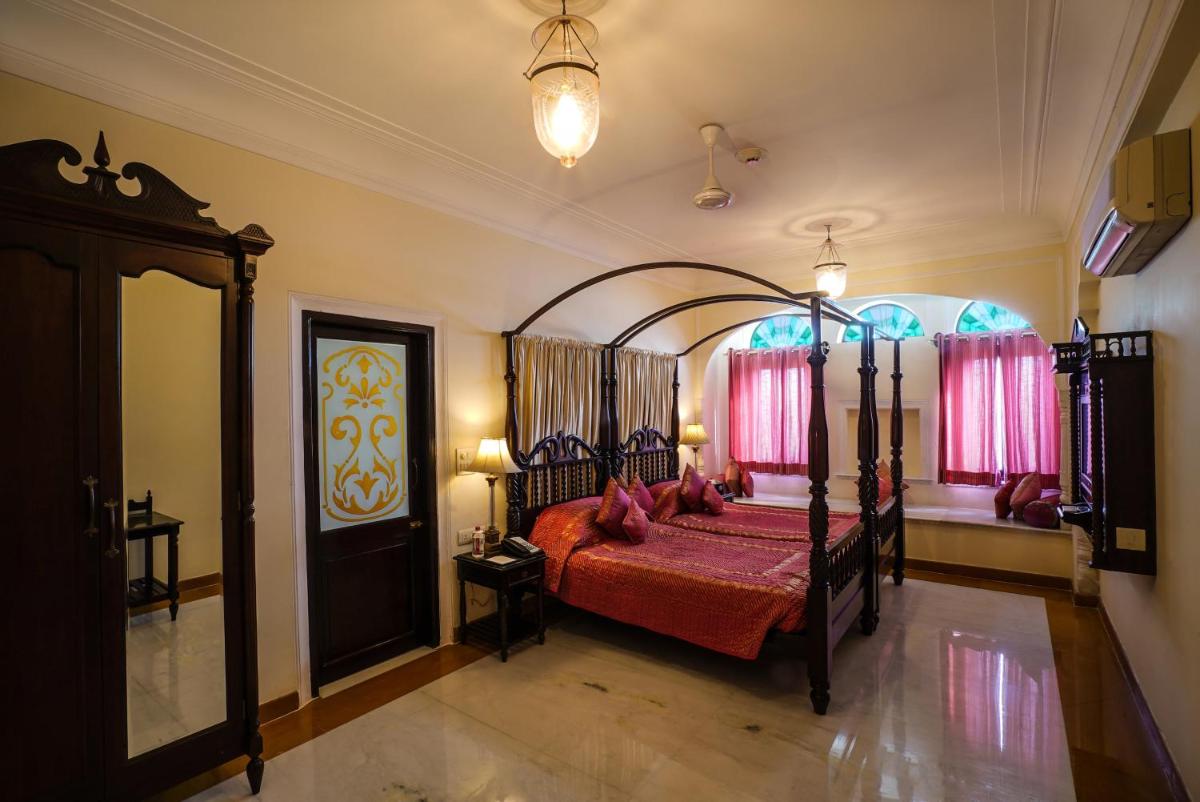 a bedroom with a bed with red sheets and pink curtains at Shahpura House in Jaipur