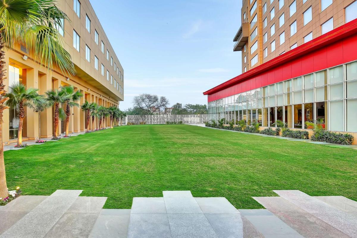 a large lawn in front of a building with palm trees at Radisson RED Chandigarh Mohali in Chandīgarh