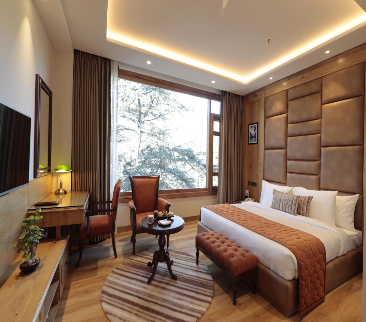 a hotel room with a bed and a desk and a table at WelcomHeritage Elysium Resort & Spa in Shimla
