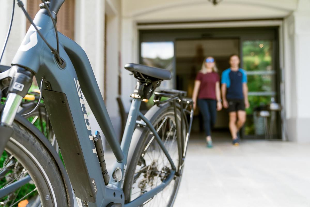 un vélo garé en face d'un immeuble avec deux personnes marchant dans l'établissement Hotel Le Cottage Bise, à Talloires