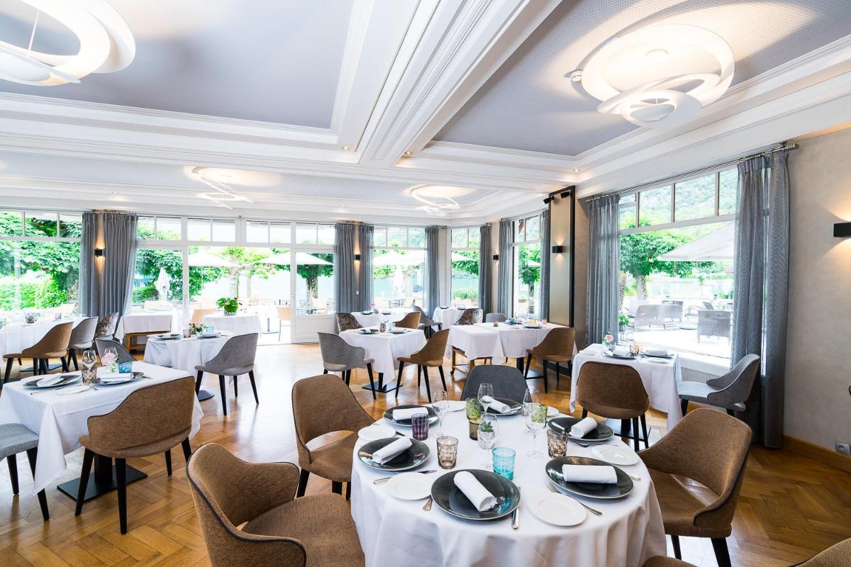 un restaurant avec des tables et des chaises blanches et des fenêtres dans l'établissement Hotel Le Cottage Bise, à Talloires