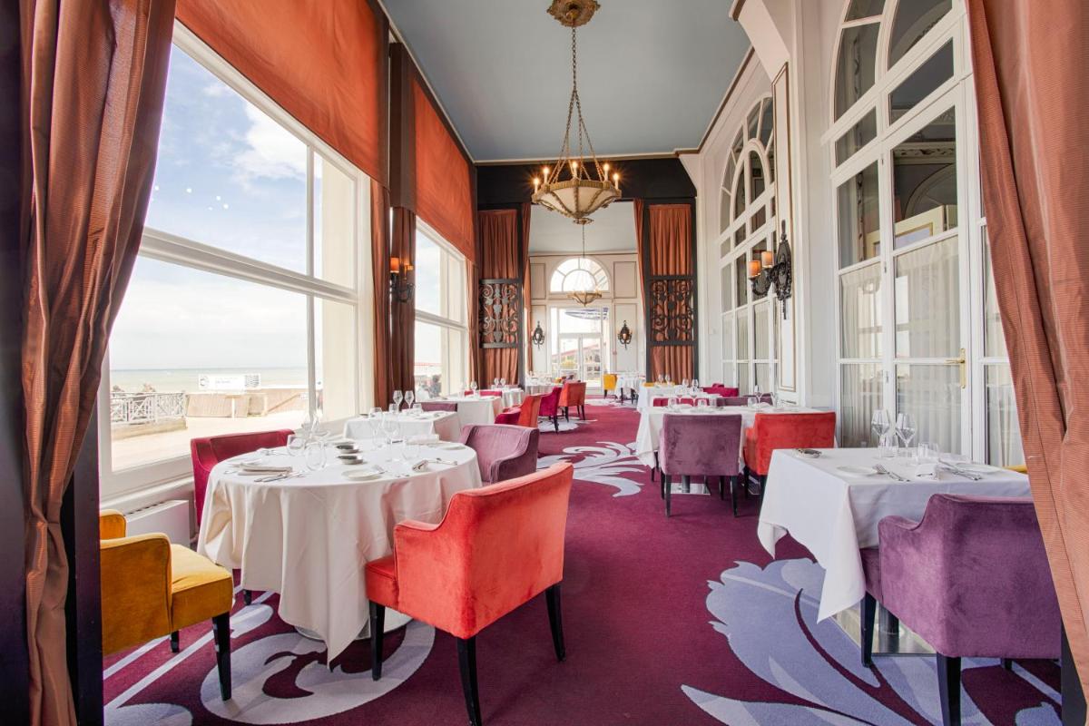 un restaurant avec des tables et des chaises et de grandes fenêtres dans l'établissement Le Grand Hotel de Cabourg - MGallery Collection, à Cabourg