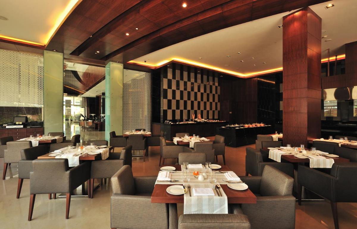 a dining room with tables and chairs in a restaurant at The Anya Hotel-Golf Course Road in Gurgaon a dining room with tables and chairs in a restaurant at The Anya Hotel-Golf Course Road in Gurgaon