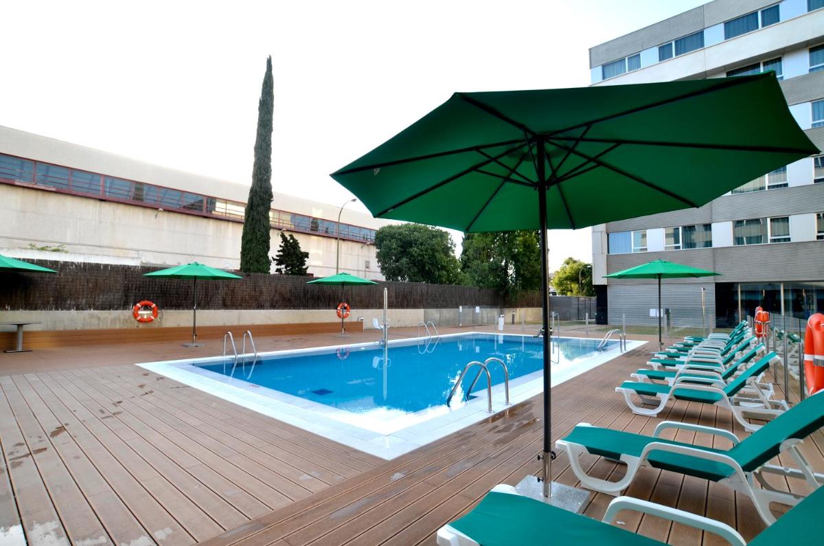 una piscina con sillas y sombrilla en Axor Barajas, en Madrid