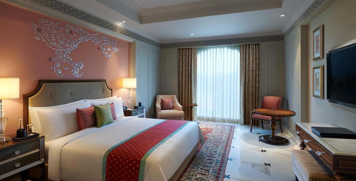 a hotel room with a large bed and a desk at The Leela Palace Jaipur in Jaipur