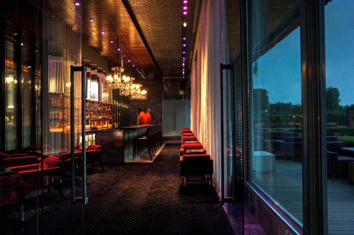 a restaurant with a bar with red chairs and windows at Taj Palace, New Delhi in New Delhi a restaurant with a bar with red chairs and windows at Taj Palace, New Delhi in New Delhi