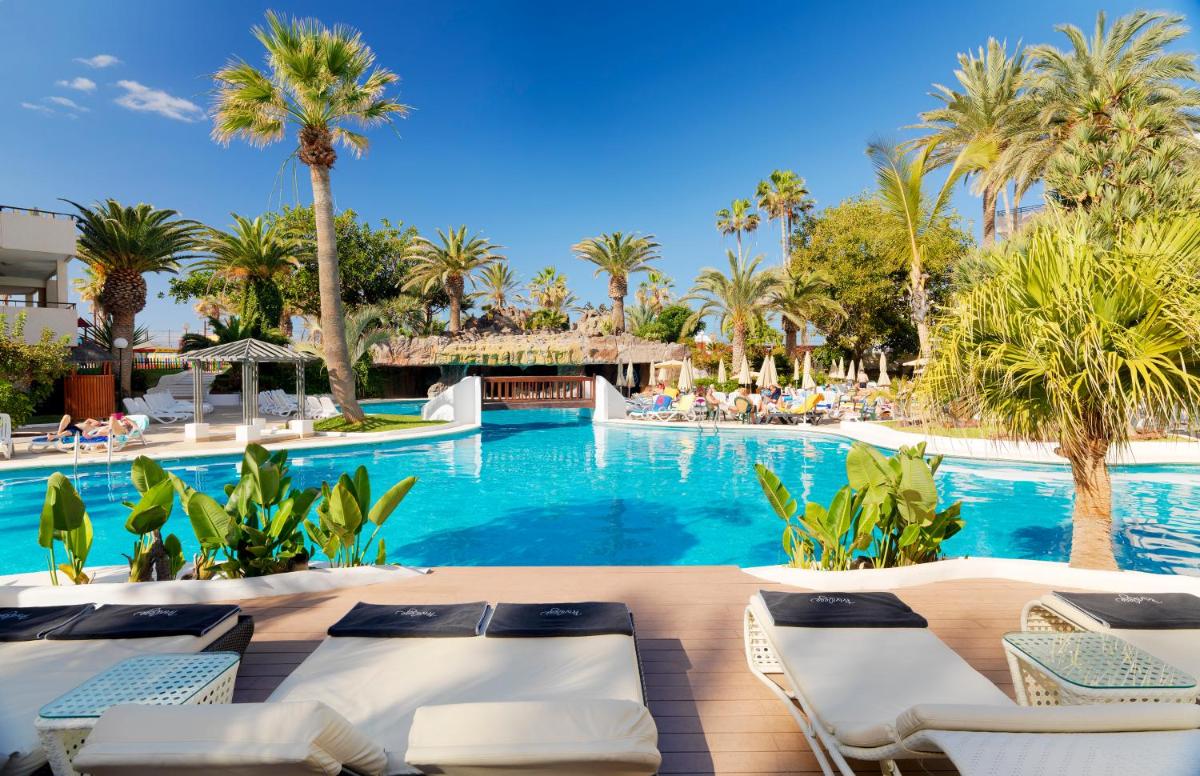 una piscina con tumbonas y palmeras en H10 Conquistador, en Playa de las Américas