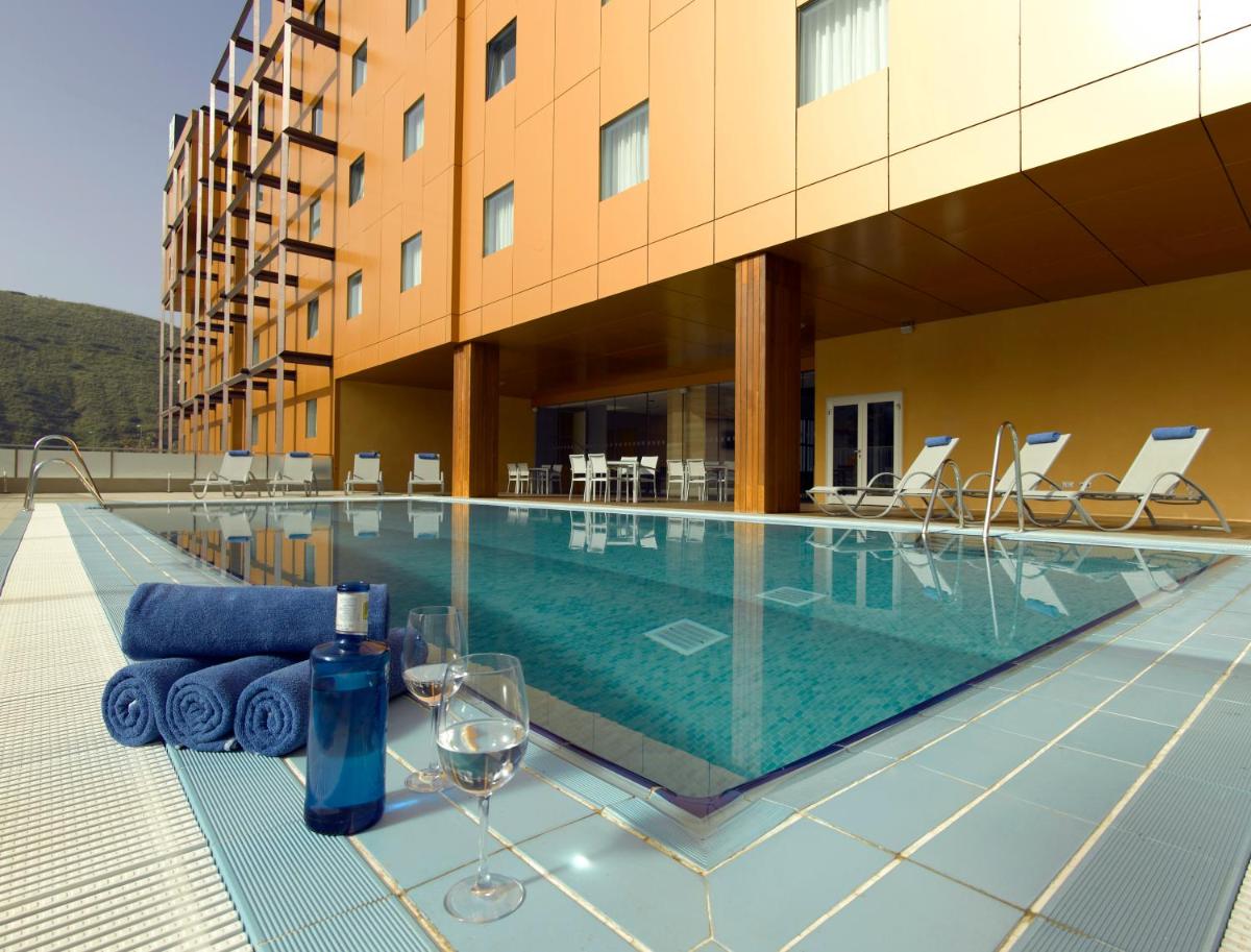 Una piscina con copas de vino y sillas al lado de un edificio. en Hotel Macià Real De La Alhambra, en Granada