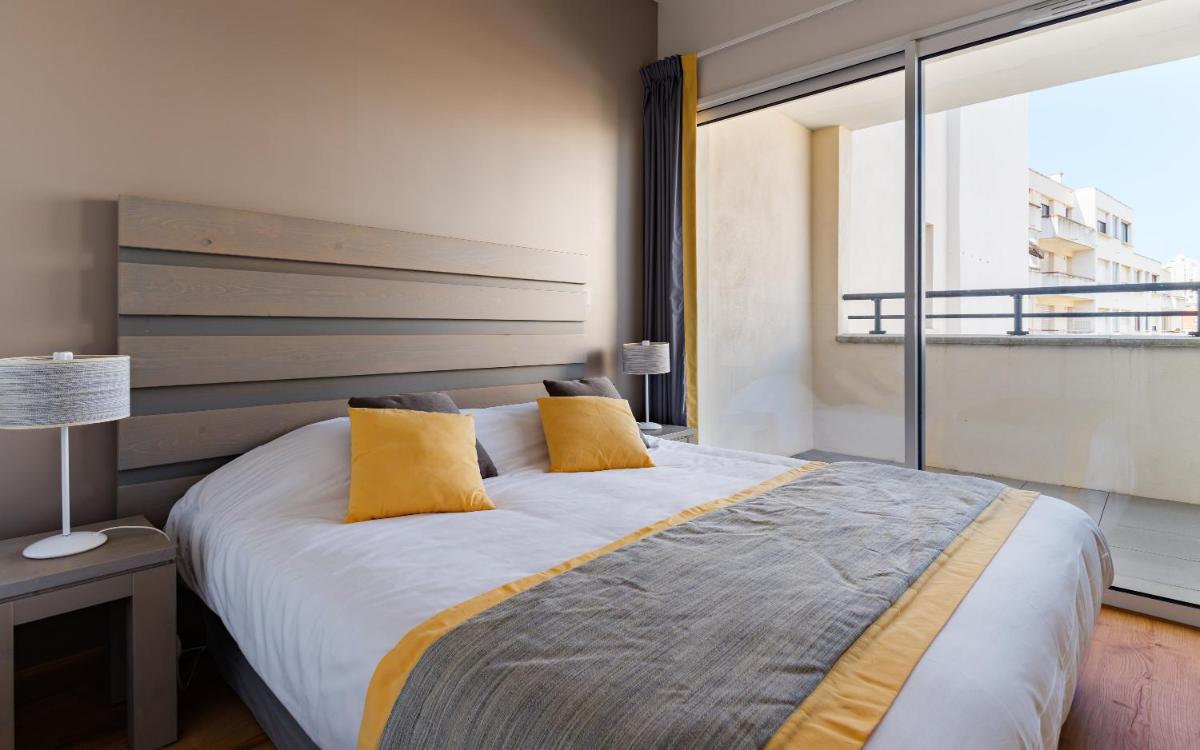 une chambre avec un grand lit avec des oreillers jaunes dans l'établissement Lagrange Vacances Les Patios Eugénie, à Biarritz