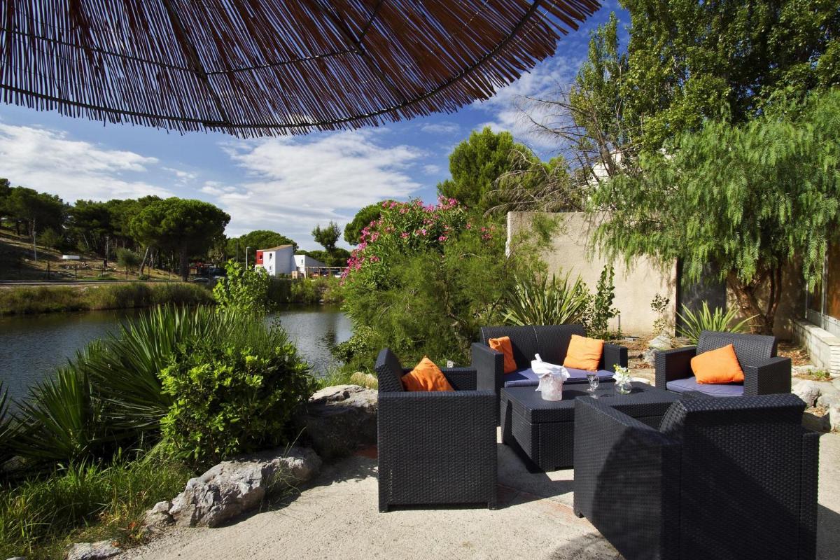 une terrasse avec des canapés et une rivière dans l'établissement Hotel Le Phoebus Garden & Spa, à Gruissan