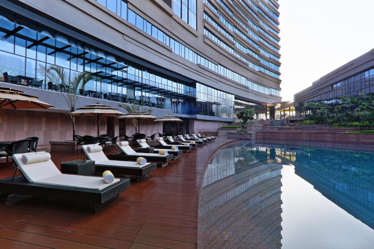 a hotel with a pool and lounge chairs next to a building at Novotel Kolkata Hotel and Residences in Kolkata a hotel with a pool and lounge chairs next to a building at Novotel Kolkata Hotel and Residences in Kolkata
