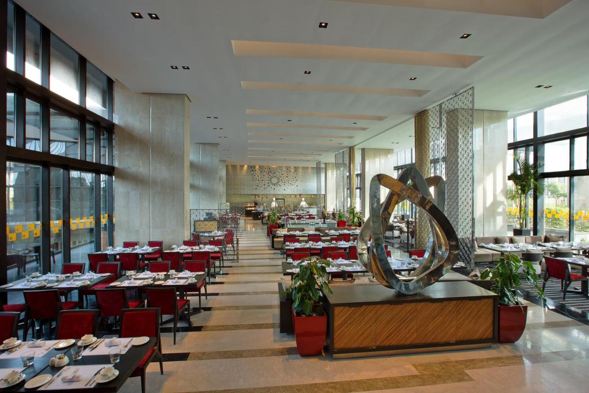 a dining room with tables and red chairs at Novotel Kolkata Hotel and Residences in Kolkata a dining room with tables and red chairs at Novotel Kolkata Hotel and Residences in Kolkata
