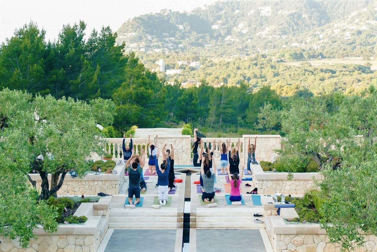 un grupo de personas haciendo yoga en un jardín en CAP VERMELL GRAND HOTEL, en Canyamel