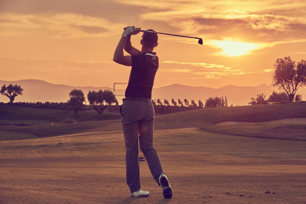 Un hombre balanceando un palo de golf en un campo de golf en CAP VERMELL GRAND HOTEL, en Canyamel