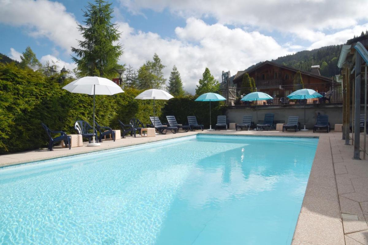 une grande piscine avec chaises et parasols dans l'établissement Loc'Hotel Alpen Sports, aux Gets