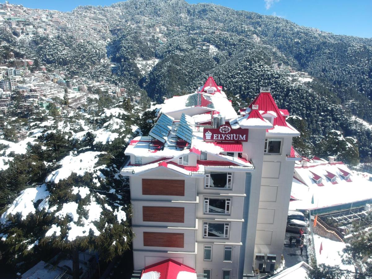 a white building with a red roof in front of a mountain at WelcomHeritage Elysium Resort & Spa in Shimla