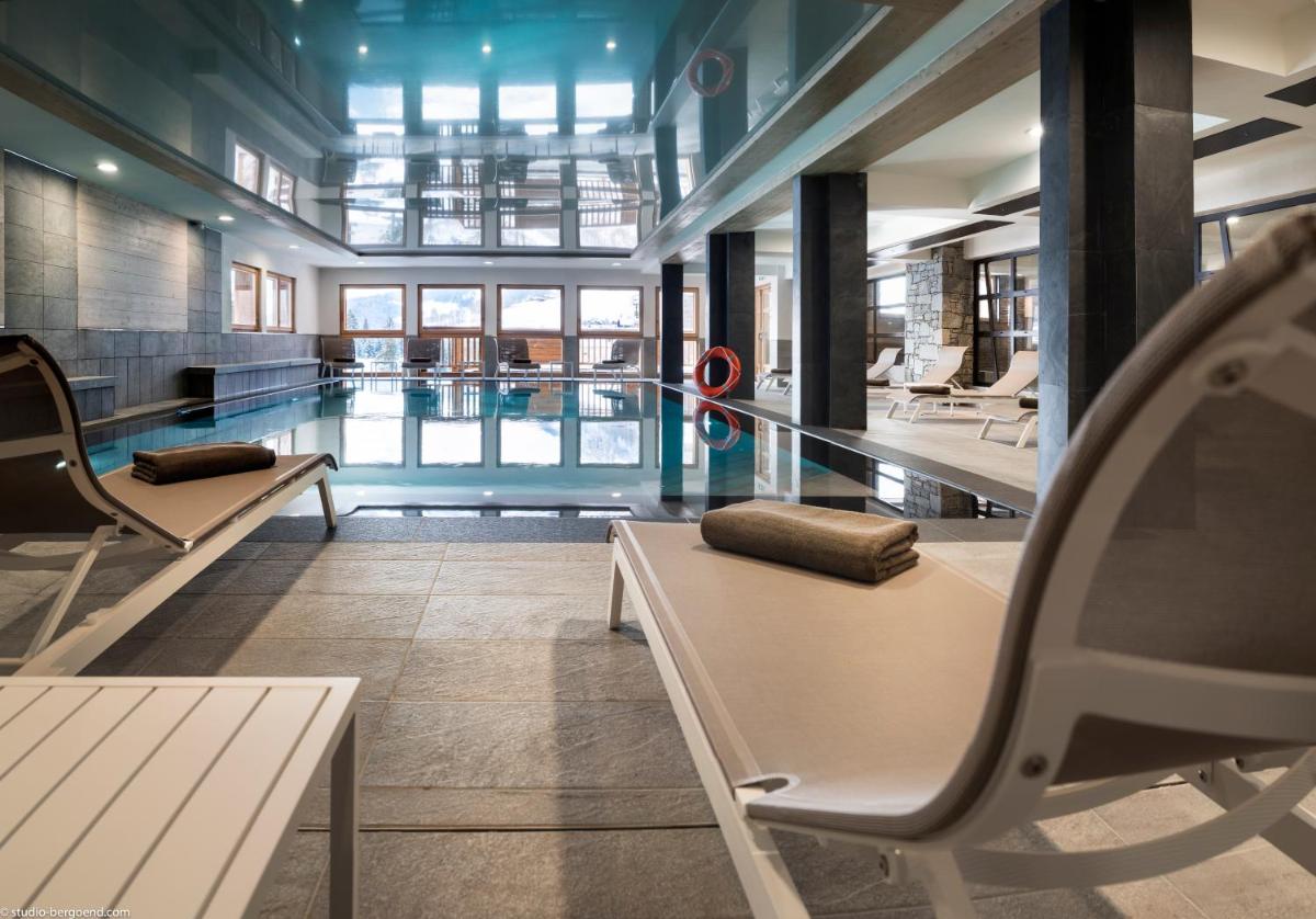 - une piscine avec des chaises et une table dans un bâtiment dans l'établissement MGM Hôtels & Résidences - Résidence Le Roc Des Tours, au Grand-Bornand