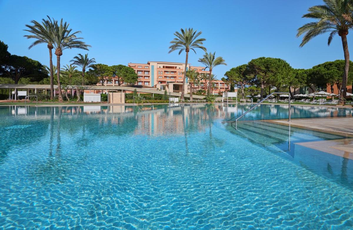 Una gran piscina con palmeras y un edificio. en Hipotels Hipocampo Palace & Spa, en Cala Millor