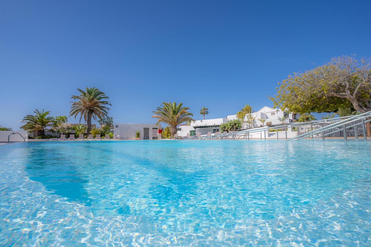 Una gran piscina con agua azul y palmeras. en Casas Heddy, Well-being Resort, en Puerto del Carmen