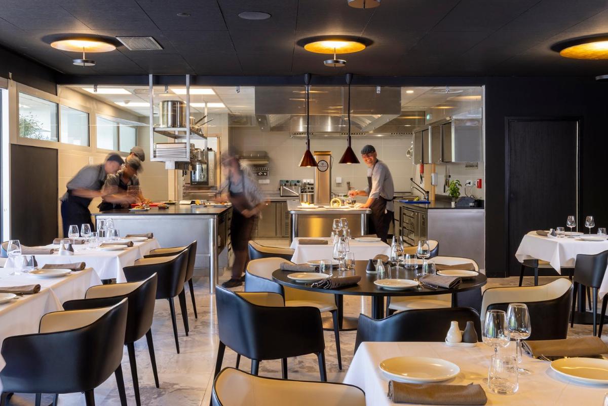 un restaurant avec des tables et des chaises et des gens dans la cuisine dans l'établissement Hôtel Spa Restaurant Villa Castellane, à Gréoux-les-Bains
