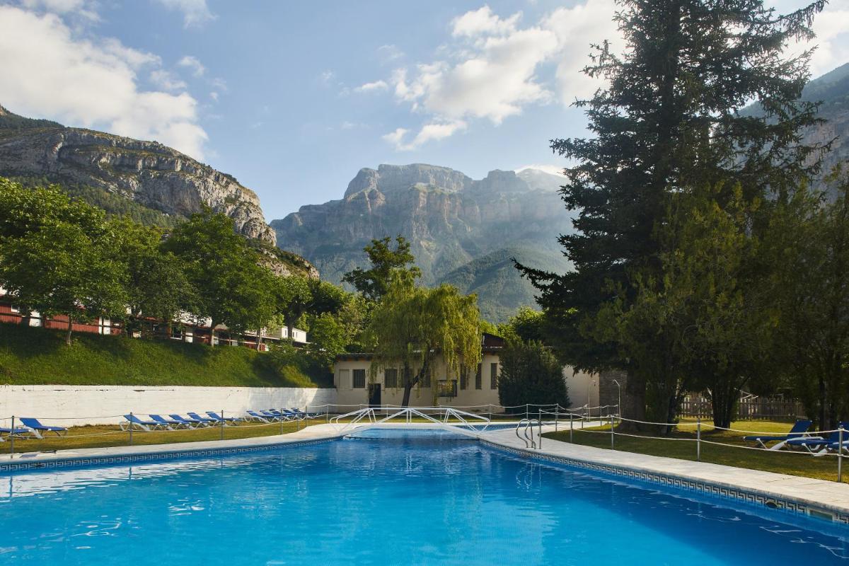 Una piscina con sillas y montañas al fondo. en Silken Ordesa, en Torla
