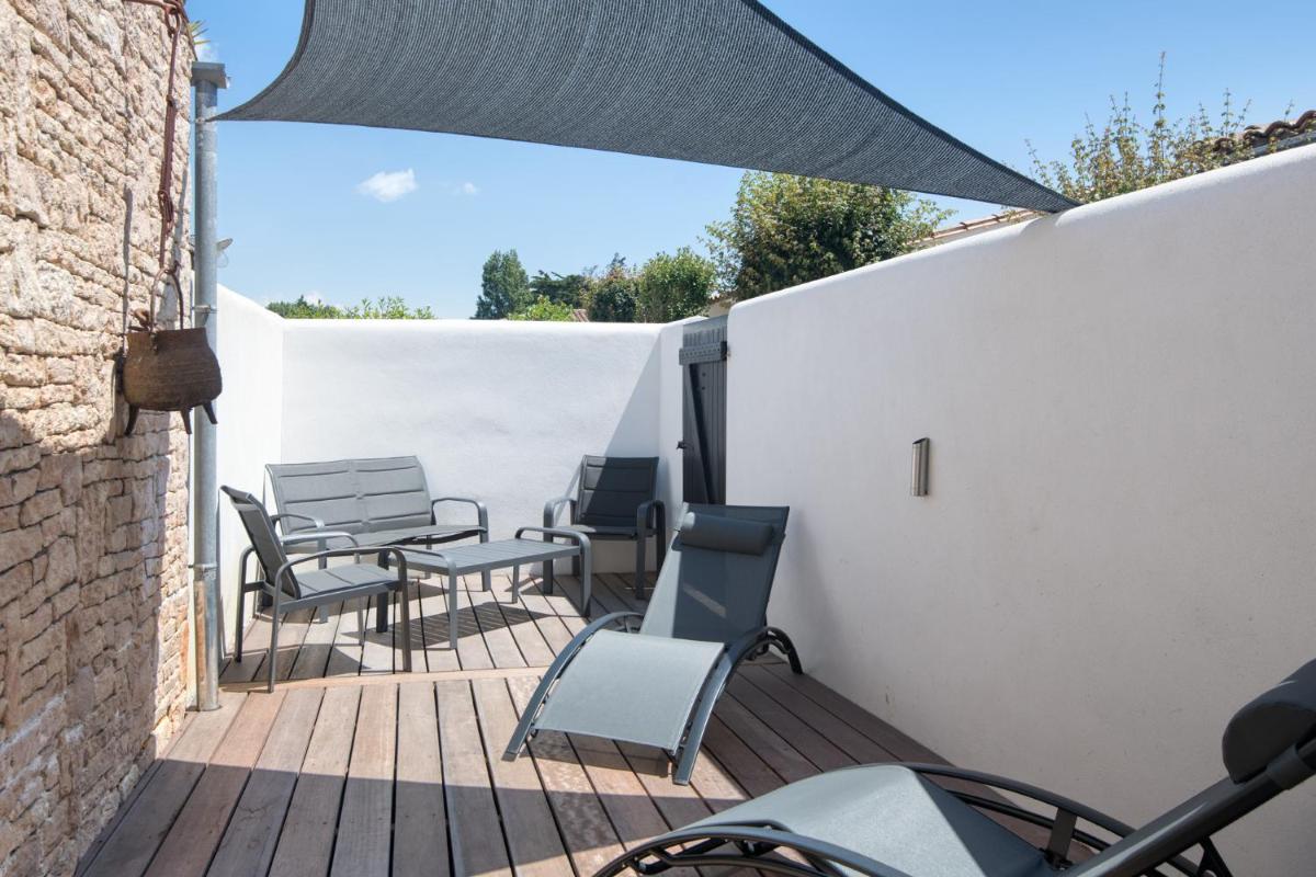 un patio avec des chaises et des tables sur un mur blanc dans l'établissement Elégance Suites Hôtel, au Bois-Plage-en-Ré