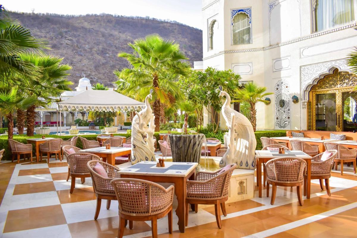 a restaurant with tables and chairs and a mountain in the background at The Leela Palace Jaipur in Jaipur