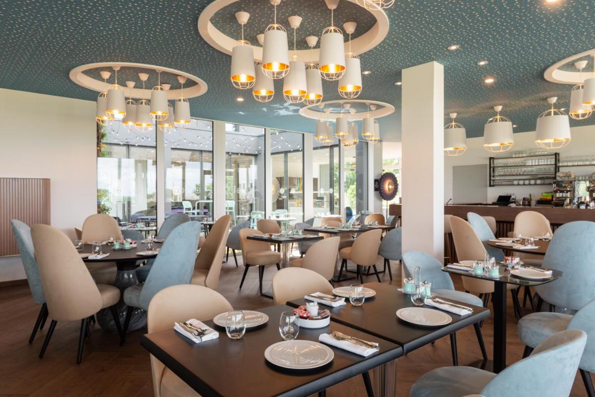 un restaurant avec des tables, des chaises et des lustres dans l'établissement Hôtel Omnubo Collection, aux Épesses