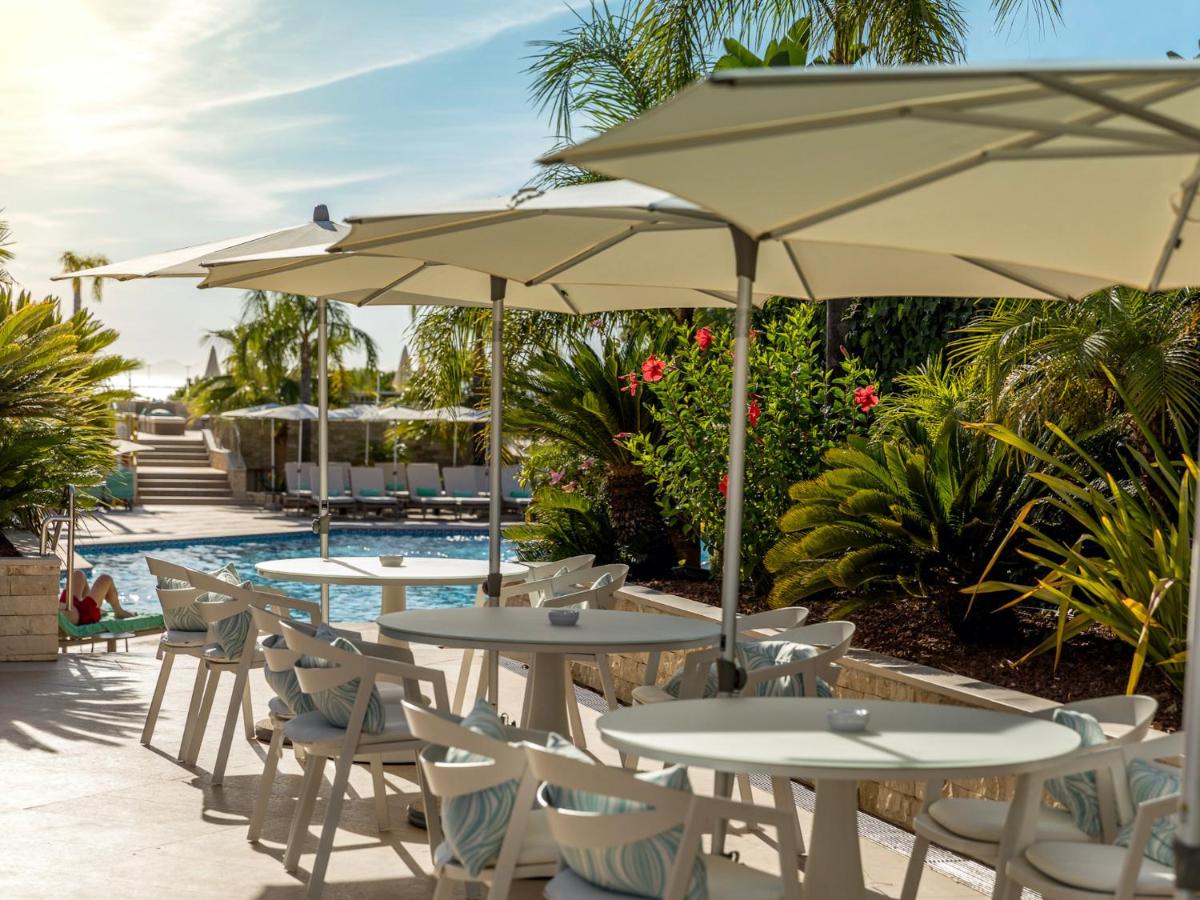 uma fila de mesas e cadeiras com guarda-sóis ao lado de uma piscina em Hotel Quinta do Lago na Quinta do Lago