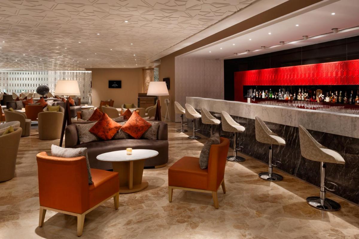 a lobby with a bar with couches and chairs at The Leela Ambience Convention Hotel Delhi in New Delhi