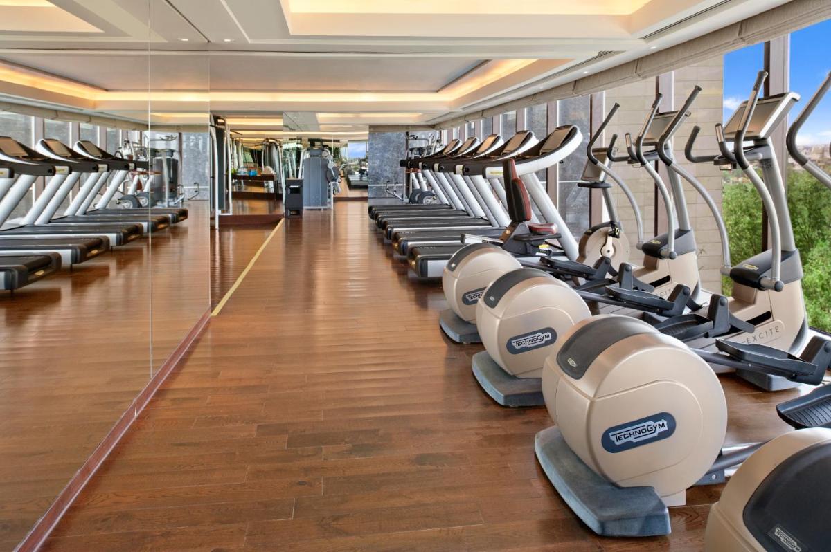 a gym with rows of treadmills and ellipticals at The Leela Ambience Convention Hotel Delhi in New Delhi
