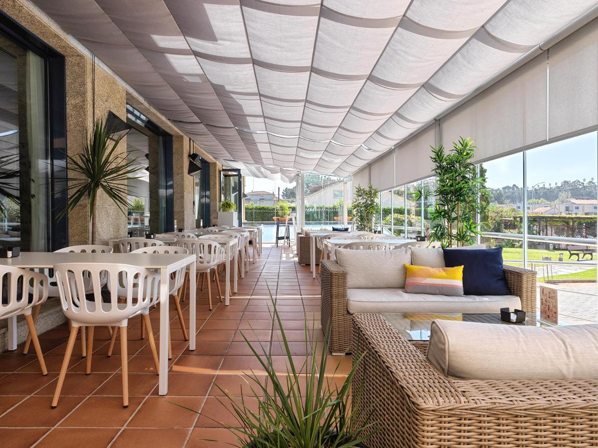 Un restaurante con mesas y sillas blancas y ventanas. en Hotel Spa Galatea, en Sanxenxo
