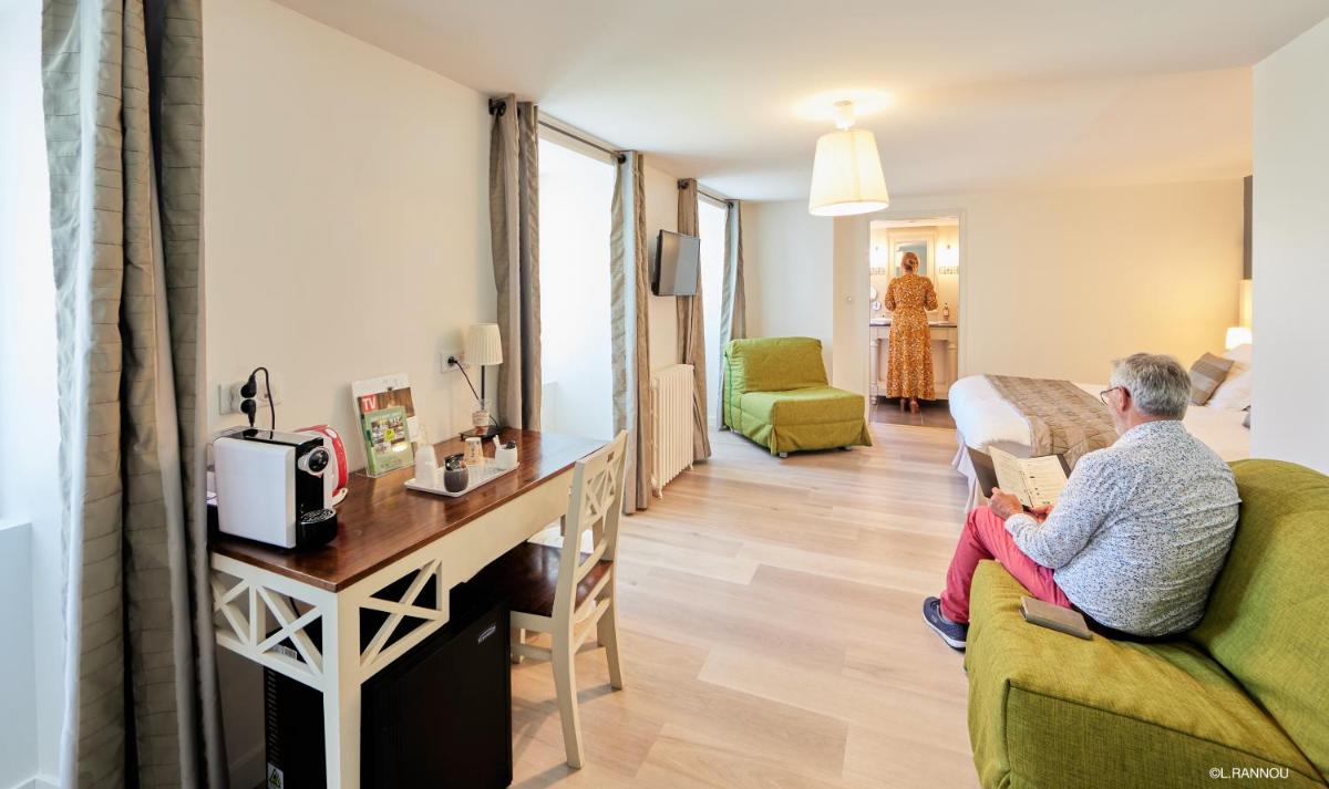 une femme assise sur un canapé dans un salon avec un ordinateur portable dans l'établissement Logis Hotel, restaurant et spa Le Relais De Broceliande, à Paimpont
