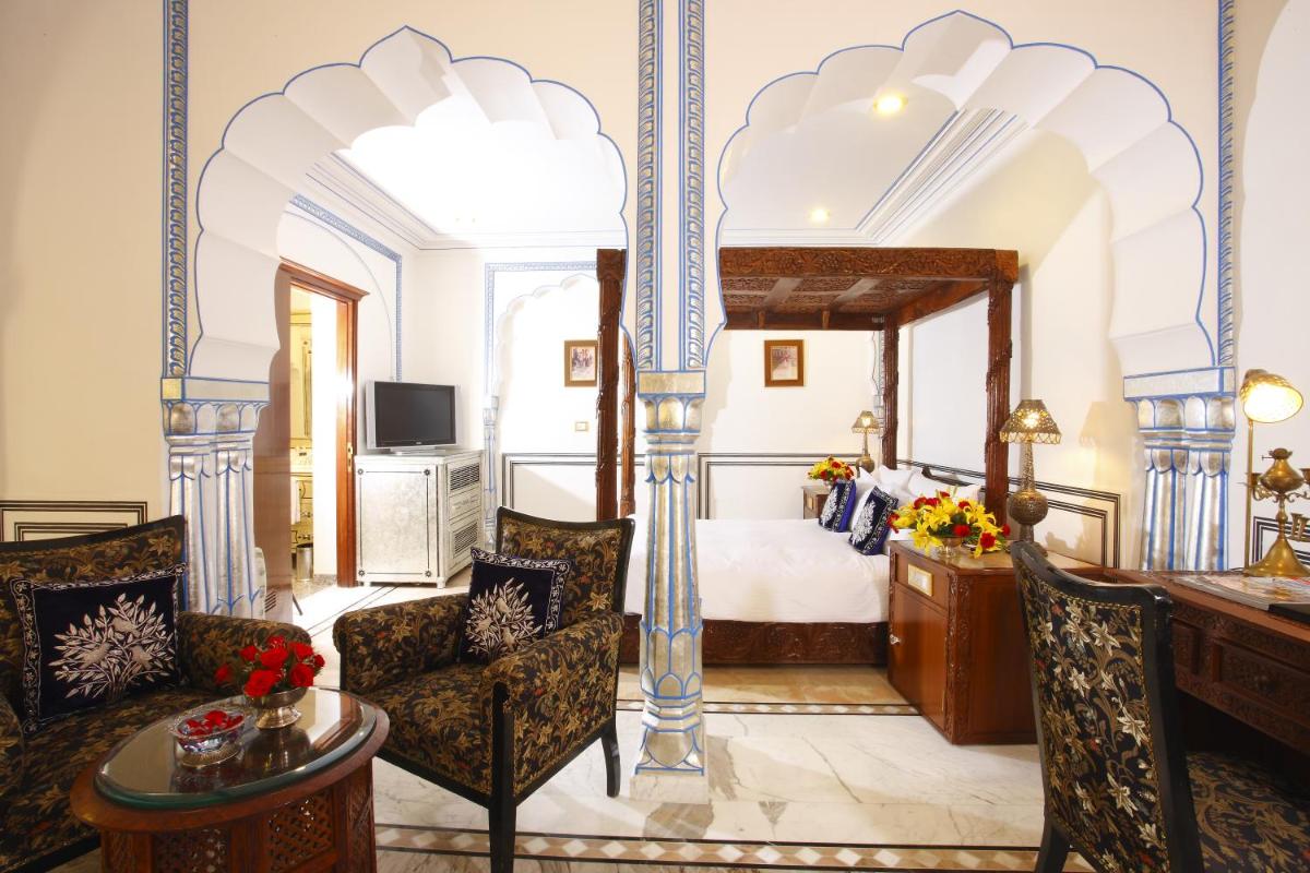a hotel room with a bed and a desk and chairs at The Raj Palace (Small Luxury Hotels of the World) in Jaipur