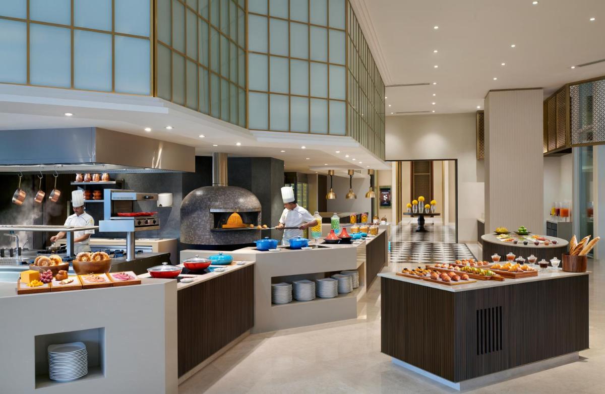 a large kitchen with people preparing food in a restaurant at The Leela Bhartiya City Bengaluru in Bengaluru a large kitchen with people preparing food in a restaurant at The Leela Bhartiya City Bengaluru in Bengaluru
