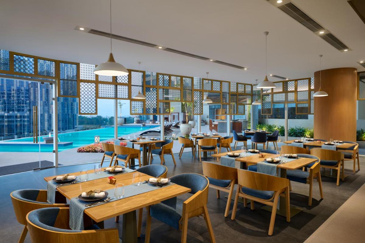 a restaurant with tables and chairs and a pool at The Leela Bhartiya City Bengaluru in Bengaluru a restaurant with tables and chairs and a pool at The Leela Bhartiya City Bengaluru in Bengaluru