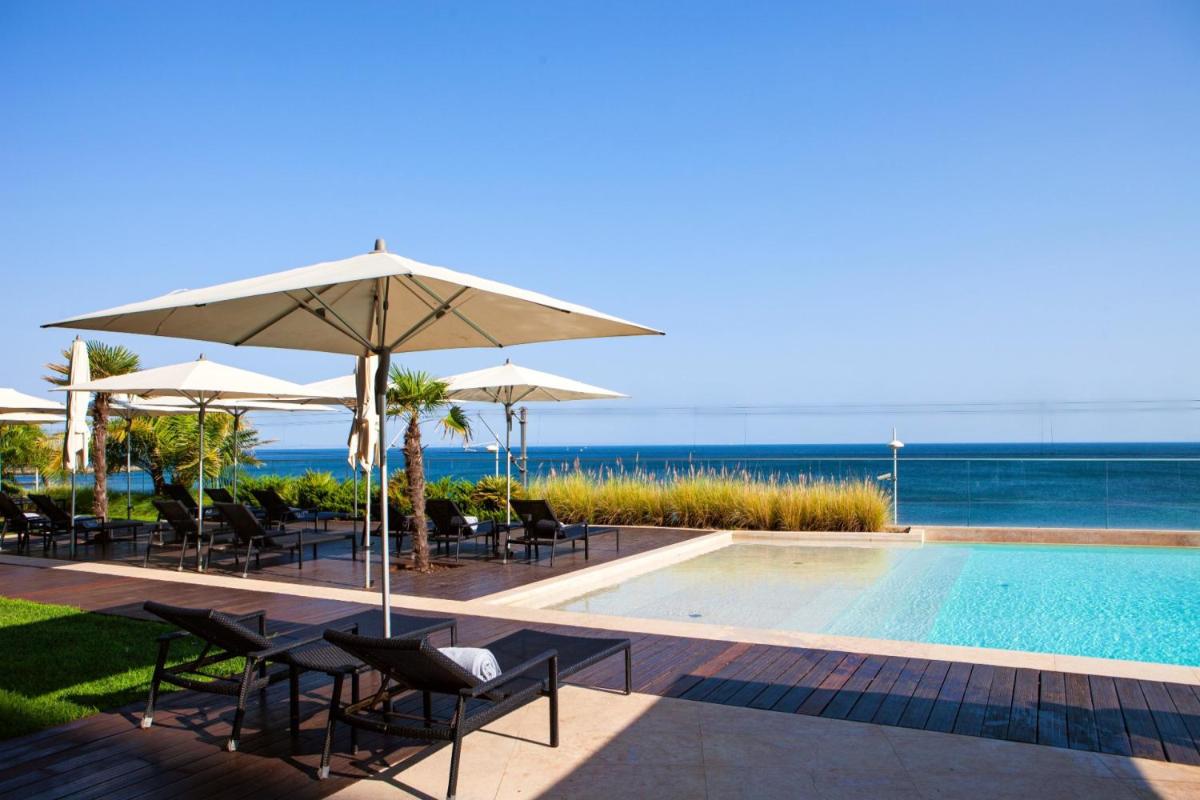 uma piscina com cadeiras e guarda-sóis junto ao oceano em InterContinental Cascais-Estoril by IHG em Estoril