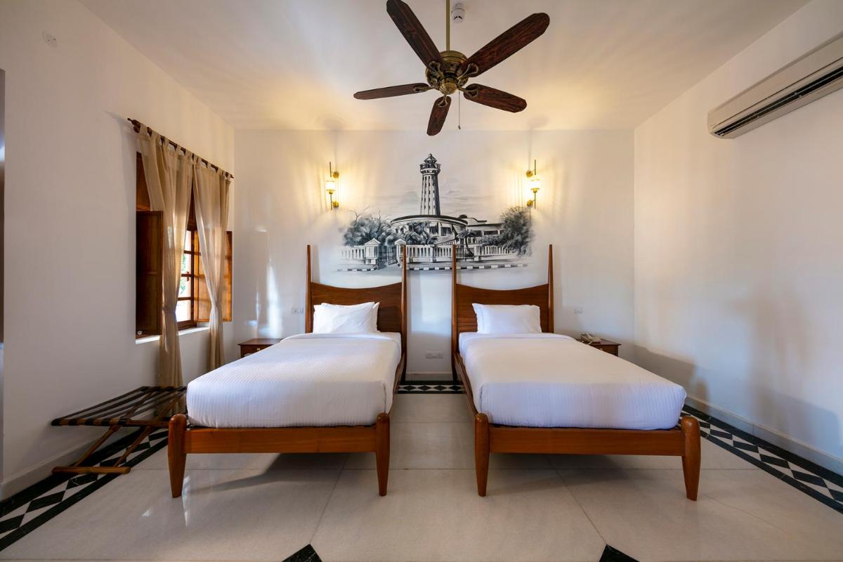 two beds in a room with a ceiling fan at Grand Hotel D'Europe in Puducherry