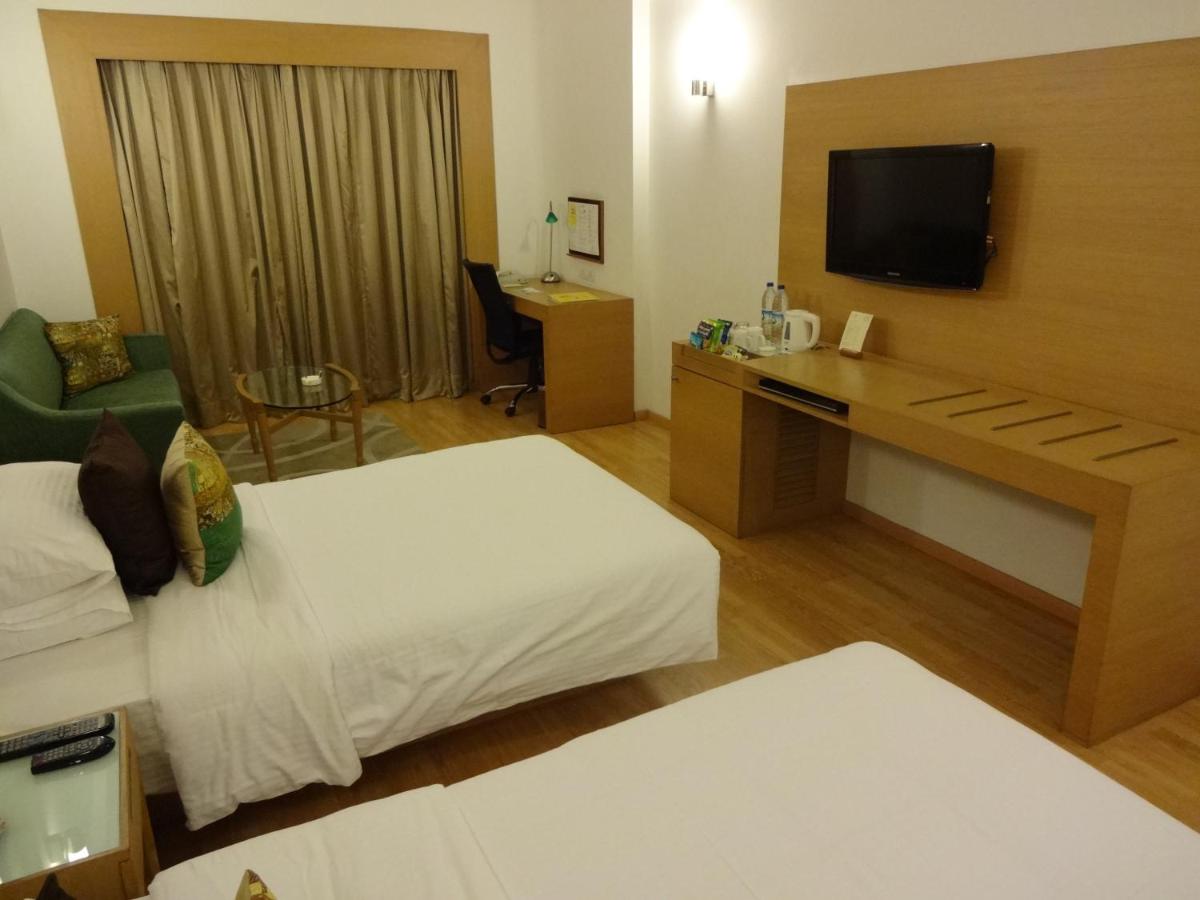 a hotel room with two beds and a desk with a television at Lemon Tree Premier Hitec City Hyderabad in Hyderabad