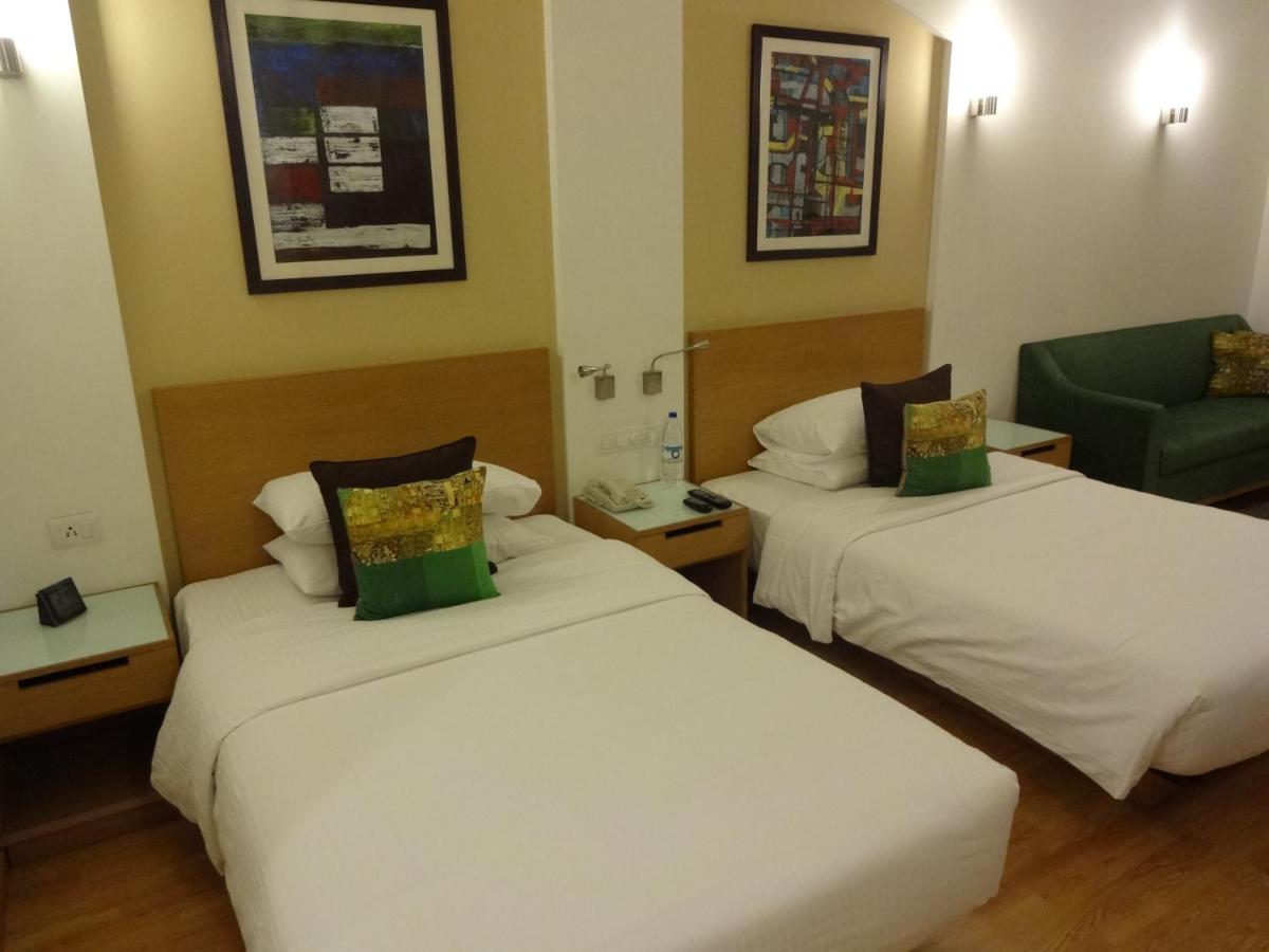 a hotel room with two beds and a green chair at Lemon Tree Premier Hitec City Hyderabad in Hyderabad