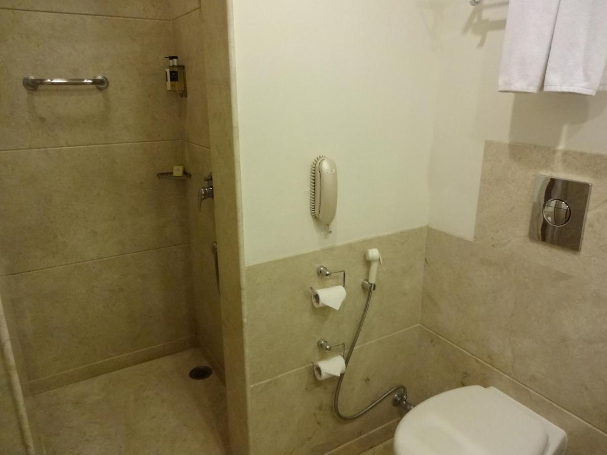 a bathroom with a shower with a toilet and a phone at Lemon Tree Premier Hitec City Hyderabad in Hyderabad