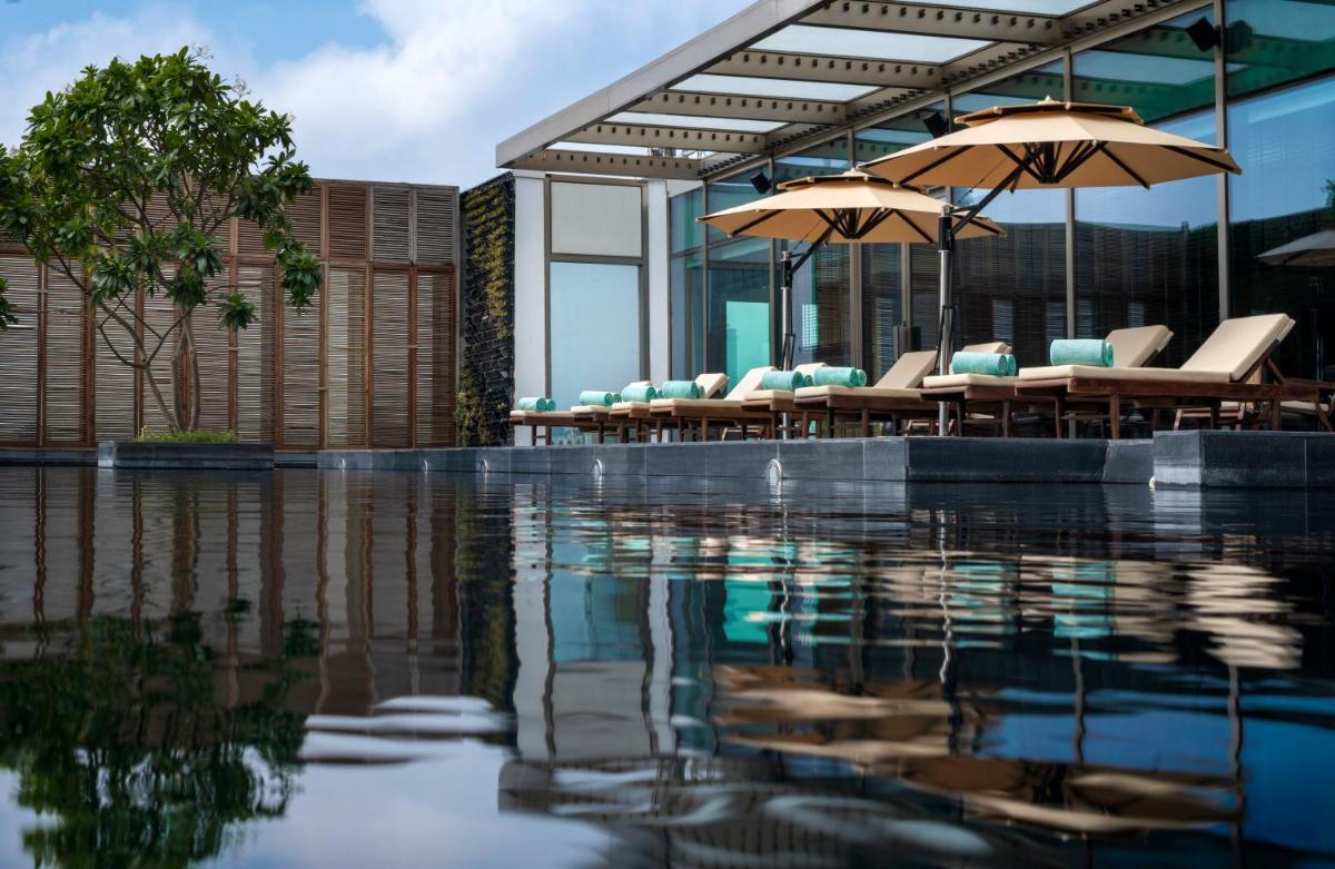 a pool of water with chairs and umbrellas at Grand Hyatt Gurgaon in Gurgaon