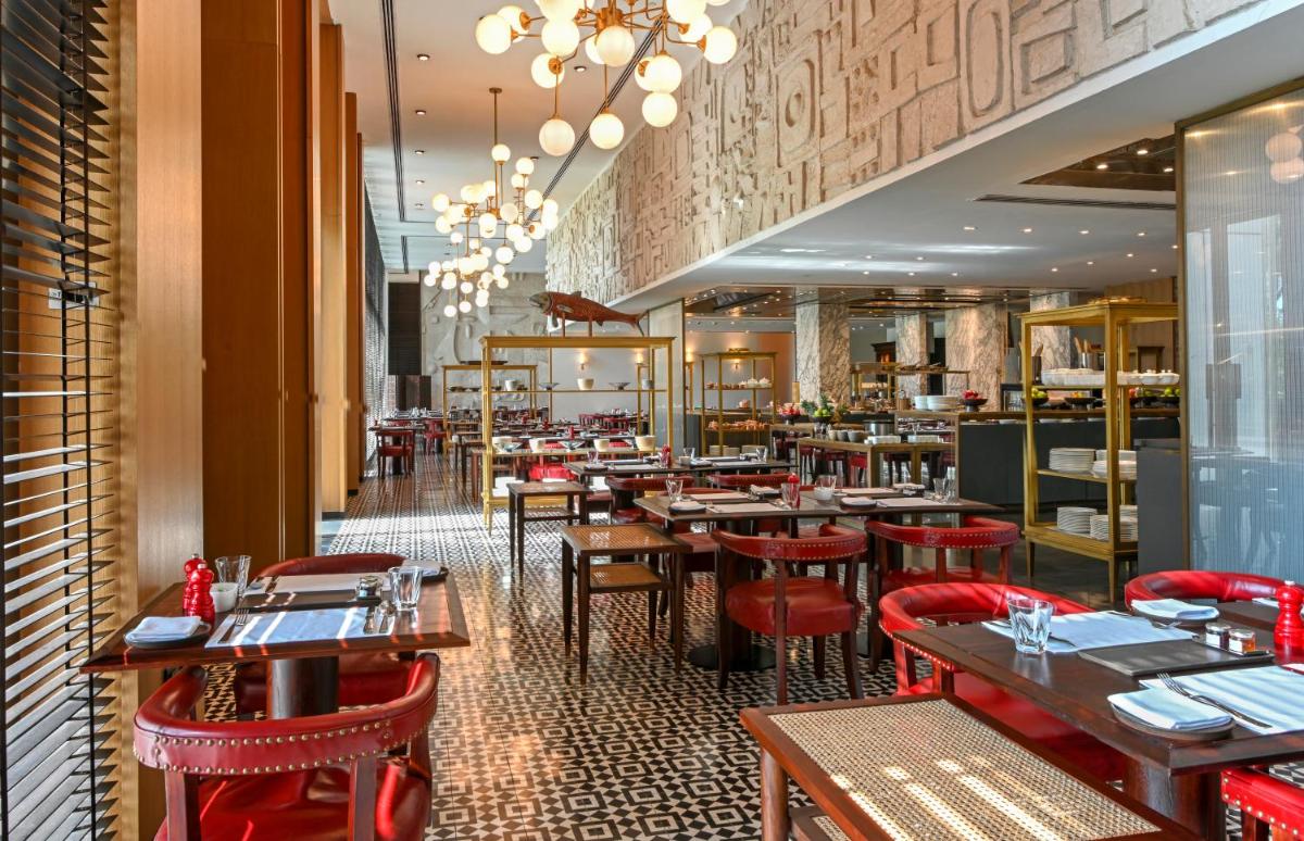 a restaurant with wooden tables and red chairs at Grand Hyatt Gurgaon in Gurgaon